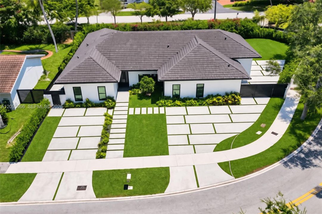 Single-story residence featuring a dark-toned tile roof, exterior white stucco finish, expansive concrete paver driveway with integrated turf ribbons, and mature privacy hedging