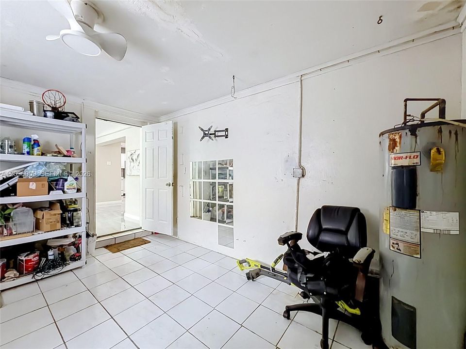 Utility room featuring tile flooring, a wall-mounted ceiling fan with integrated lighting, a glass-block accent panel, and a six-panel interior door