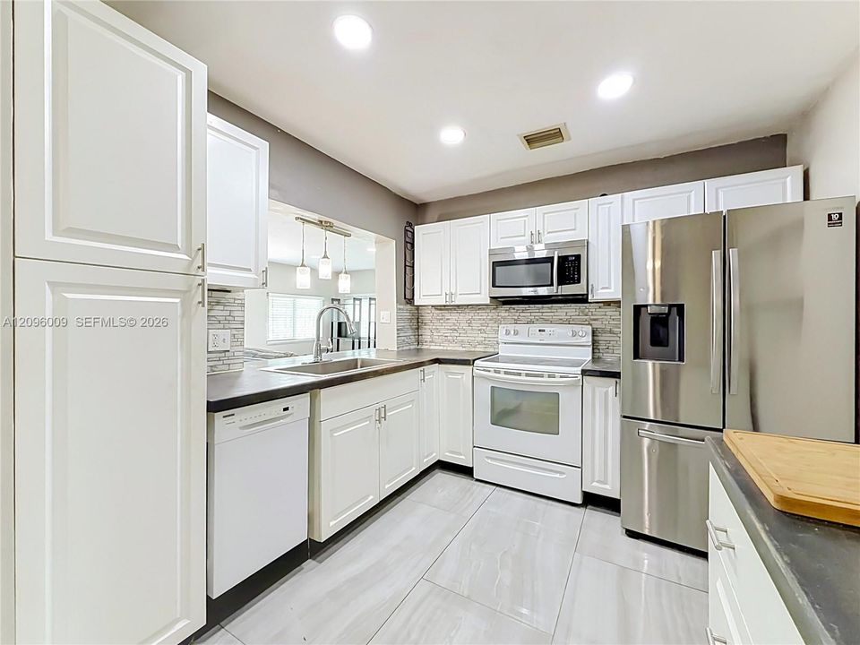 Kitchen featuring white shaker-style cabinetry, stainless steel appliances, tiled backsplash, dark solid-surface countertops, and large-format tile flooring