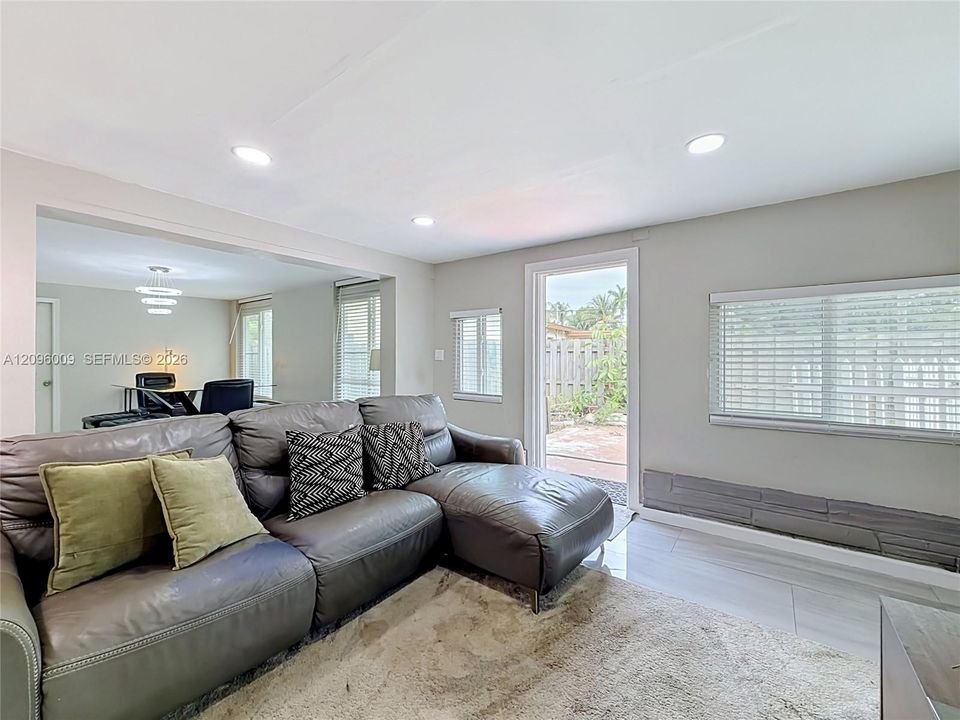 Light-filled interior featuring smooth-finish ceilings with recessed lighting, tile flooring, large windows with horizontal blinds, and a door providing exterior access