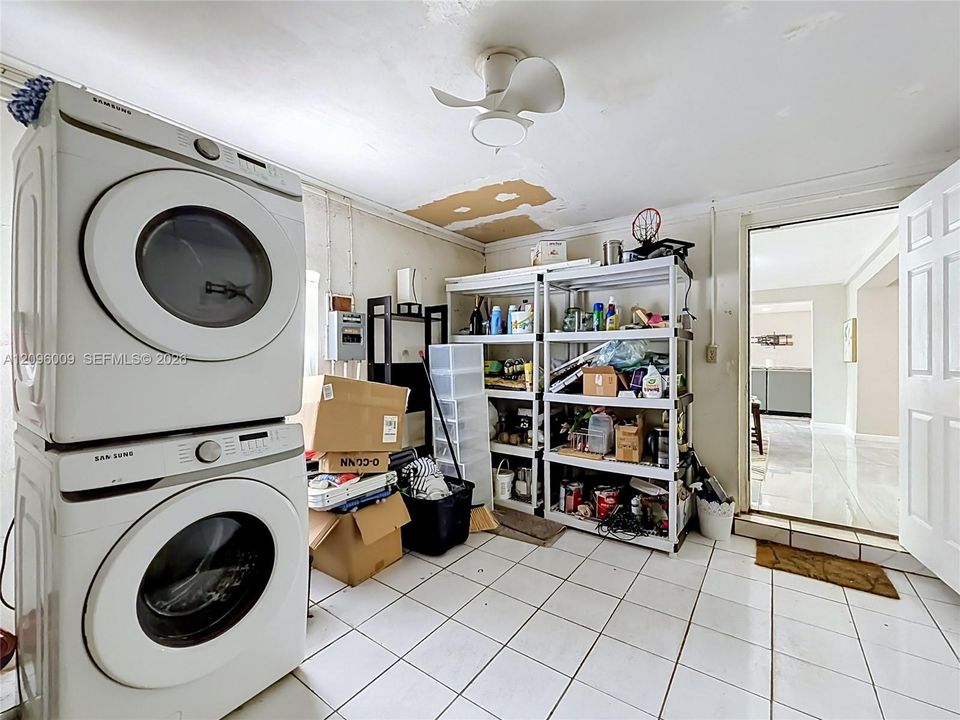 Utility area featuring white ceramic tile flooring, a ceiling-mounted fan, and a stacked front-load laundry appliance set