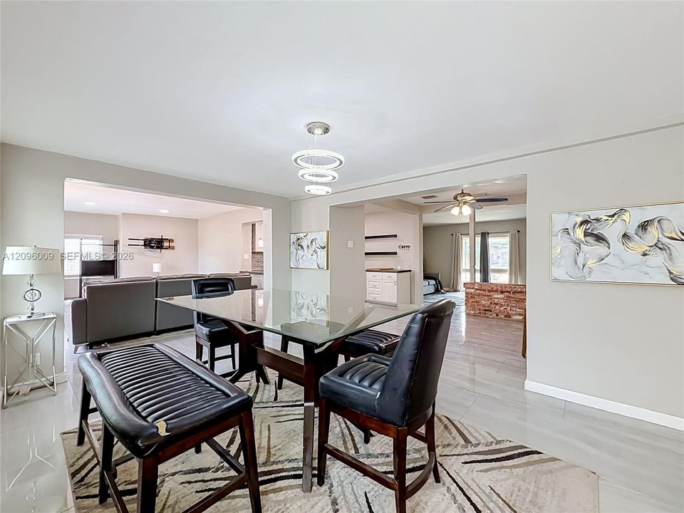 Open-concept dining area featuring neutral wall tones, large-format tile flooring, a multi-tiered circular pendant light fixture, and a brick partition wall