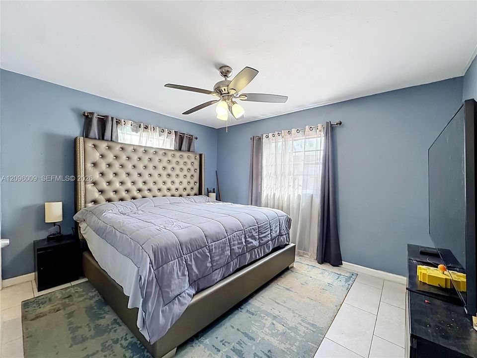 Light-filled room featuring large windows with neutral-toned treatments, tile flooring, and a ceiling-mounted light fixture with a central fan