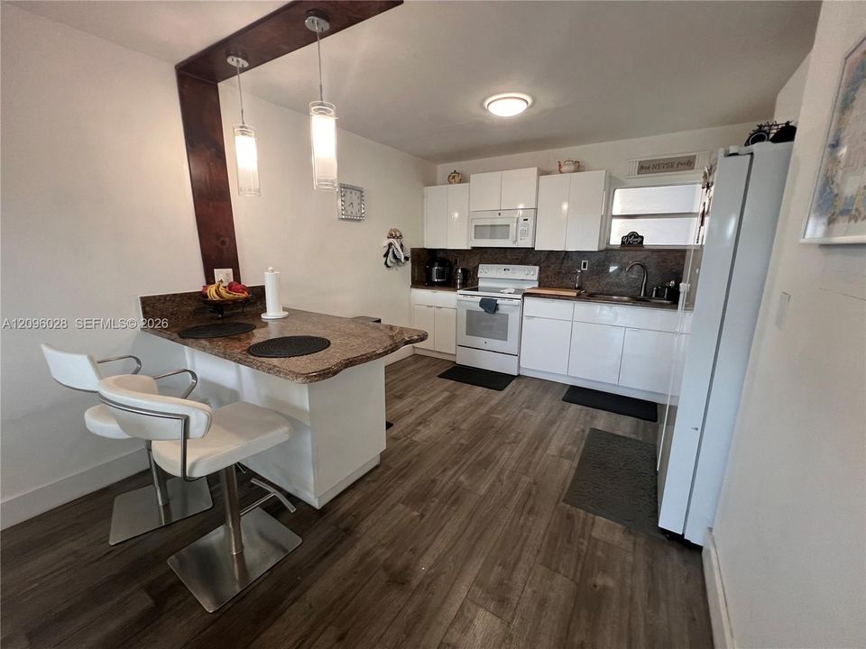 Kitchen featuring white cabinetry, stone-surface breakfast bar, wood-finish flooring, and dual hanging pendant lights