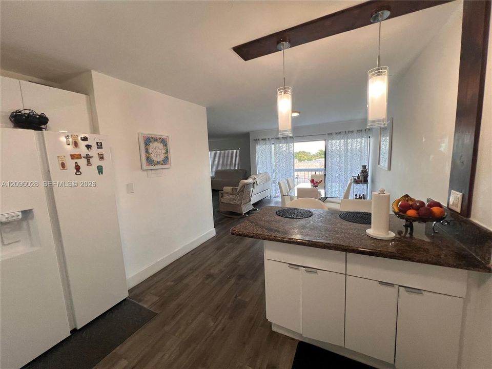 Kitchen featuring a breakfast bar with stone-finish countertop, white cabinetry, wood-finish flooring, and dual hanging pendant lights