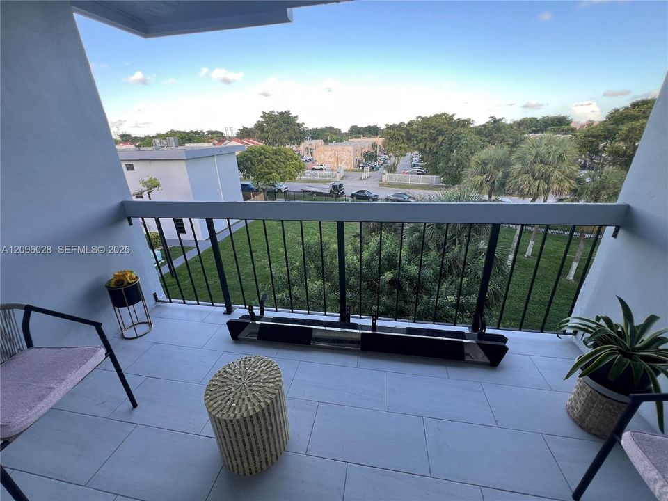 Covered balcony featuring large-format grey floor tiling, a black metal railing, and an open outdoor space
