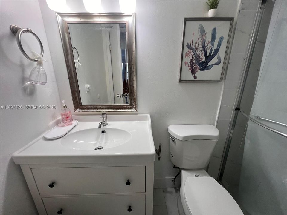 White vanity with an integrated basin, brushed metal hardware, wall-mounted mirror, overhead light fixture, and walk-in shower with sliding glass doors
