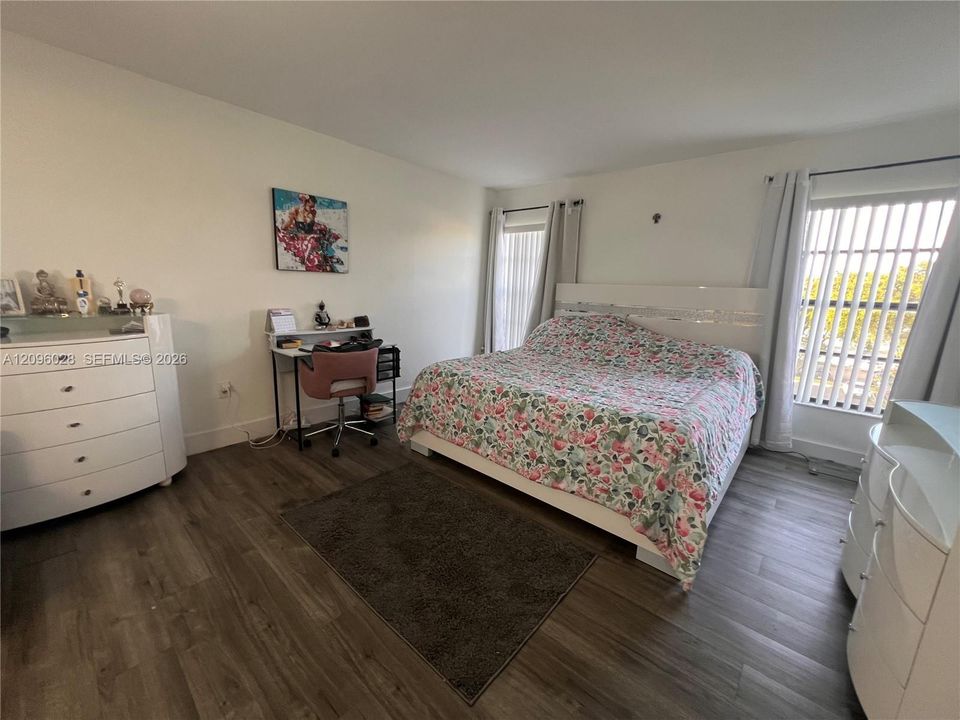 Wood-finish flooring, neutral wall tones, and large windows with vertical blinds