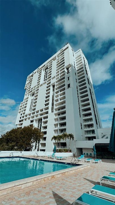 High-rise tower featuring tiered balconies and an outdoor swimming pool with paver decking