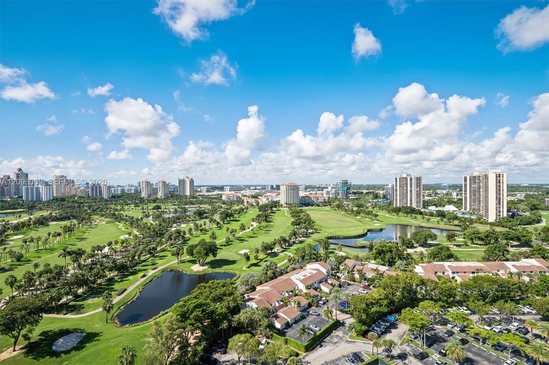 Panoramic aerial perspective featuring expansive golf course fairways, mature landscaping, integrated water features, and multi-story structural architecture