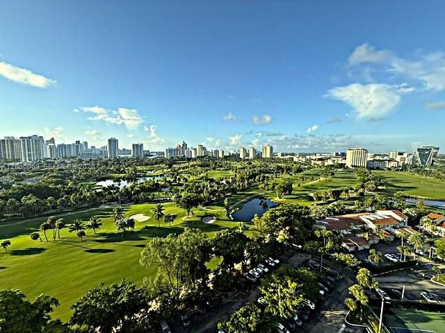 Expansive golf course grounds featuring manicured turf, multiple water hazards, mature palm trees, and an urban skyline backdrop