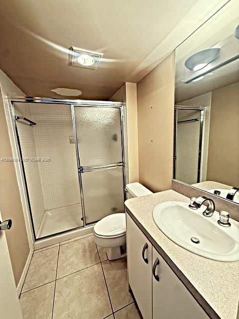 Bathroom featuring a walk-in shower with glass sliding doors and tile surround, vanity with an integrated sink and chrome faucet, large wall-mounted mirror, and tile flooring