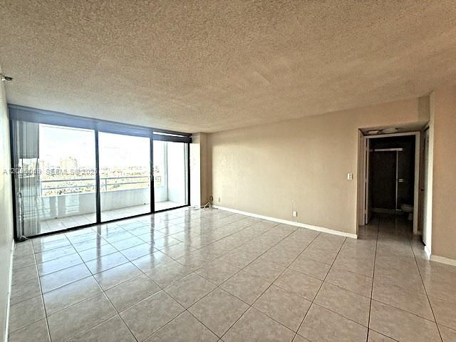 Open living area featuring large-format ceramic tile flooring, neutral wall finishes, and floor-to-ceiling sliding glass doors opening to a balcony