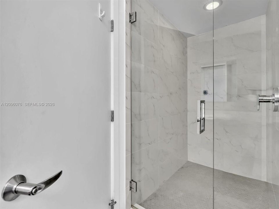 Walk-in shower featuring large-format stone-finish tile surround, frameless glass enclosure, recessed ceiling lighting, and chrome plumbing fixtures