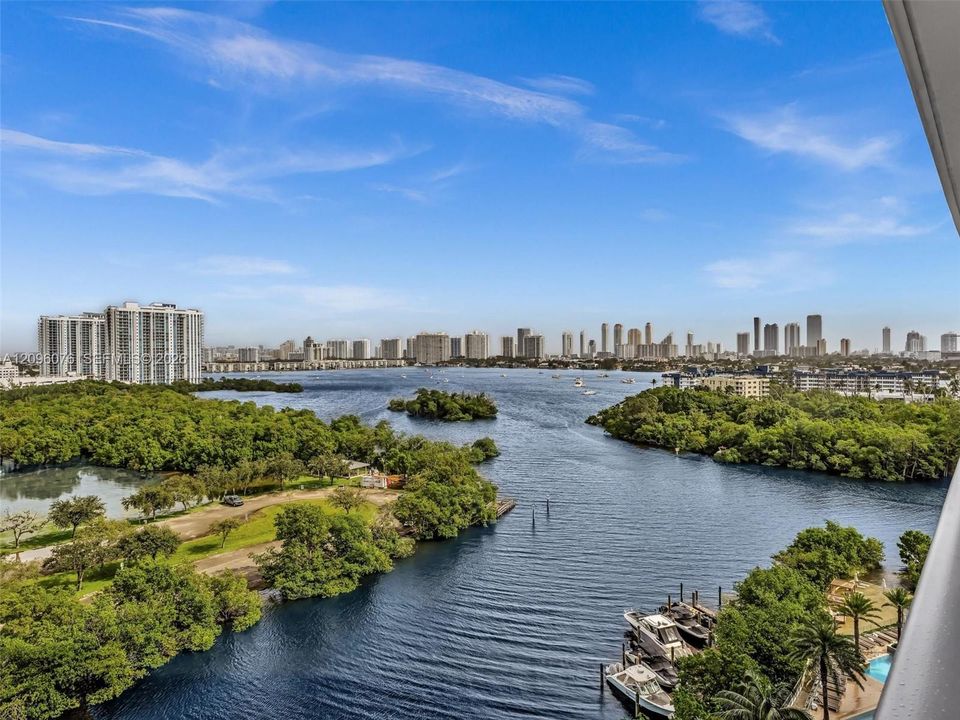 Panoramic water, island, and city skyline scenery featuring a waterway, mature vegetation, and multiple boat docks