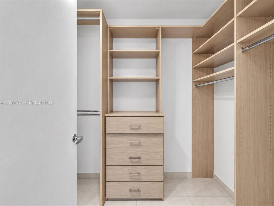 Custom walk-in closet featuring light-toned wood-finish cabinetry, built-in shelving, integrated dresser drawers, and metal hanging rods