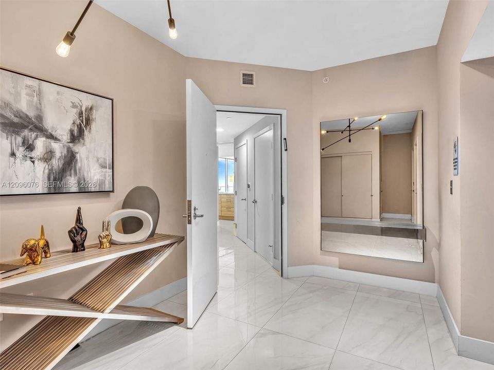 Foyer featuring polished stone-finish flooring, a wall-mounted rectangular mirror, and modern multi-arm light fixture