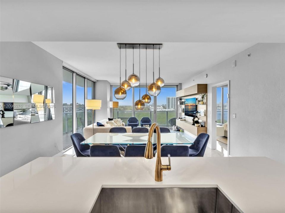 Solid surface countertops, under-mount stainless steel sink, bronze-tone faucet, multi-light pendant fixture with spherical glass shades, and floor-to-ceiling glass panel walls