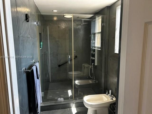 Bathroom featuring large-format dark stone tile, a glass-enclosed shower with integrated body sprays and rainfall showerhead, a wall-mounted bidet, and a low-profile toilet