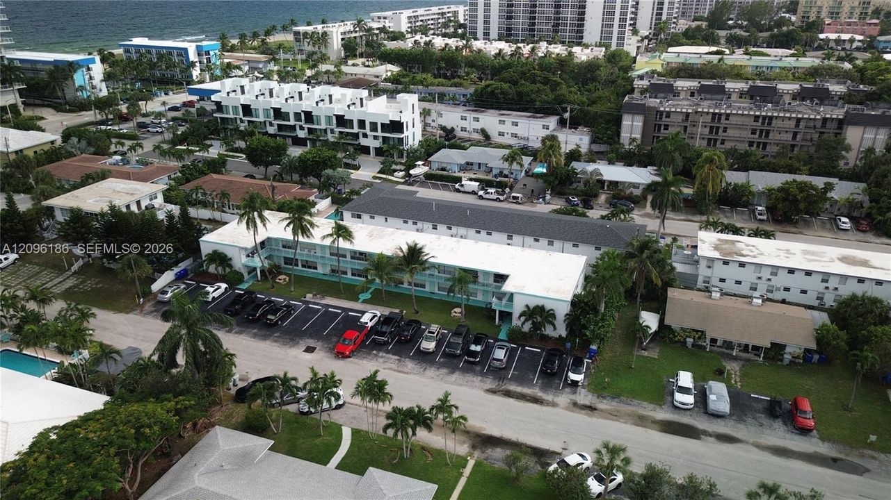 Multi-story residential structure featuring exterior walkways, a dedicated asphalt parking area, and mature palm tree landscaping