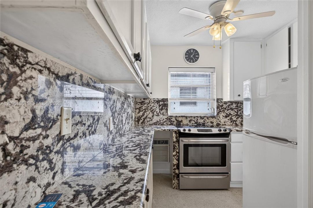 Kitchen featuring stone-patterned countertops and matching full-height backsplash, white cabinetry, stainless steel range, white refrigerator, and ceiling-mounted light fixture with fan