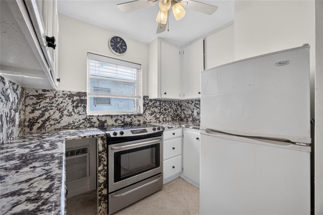 Kitchen featuring white shaker-style cabinetry, high-contrast patterned stone countertops and backsplash, stainless steel range, and ceiling-mounted light fixture