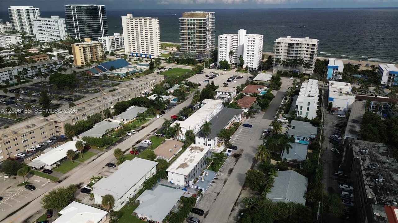Aerial perspective featuring coastal proximity, multi-story building density, expansive paved parking lots, mature palm trees, and established street-level infrastructure