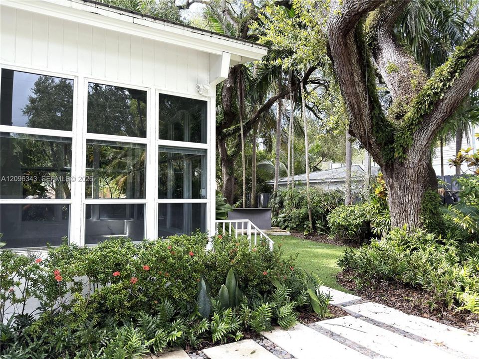 Bright sun room spills to landscaped yard with turf and concrete landing paths