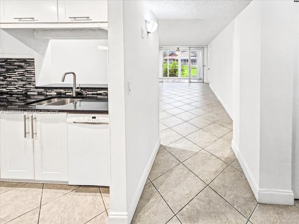 Kitchen featuring white cabinetry, dark countertops, a mosaic tile backsplash, and stainless steel hardware, set against diagonal-set stone-finish tile flooring
