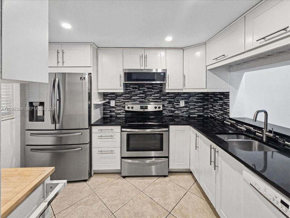 Kitchen featuring white shaker-style cabinetry, dark stone countertops, stainless steel appliances, a mosaic tile backsplash, and recessed lighting