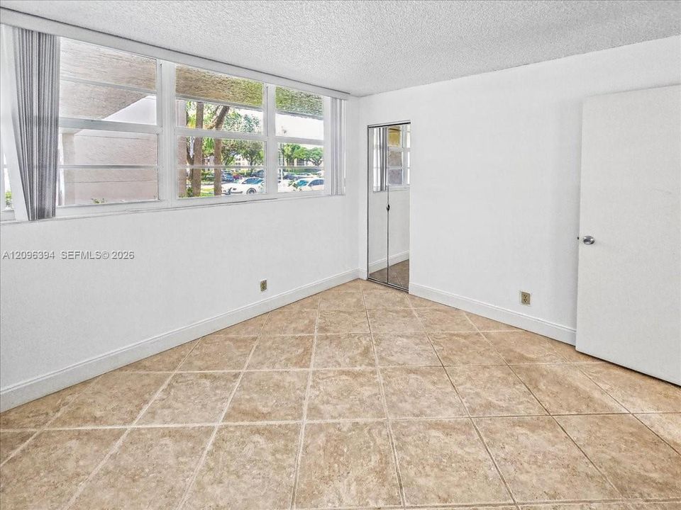 Neutral-toned tiled flooring, floor-to-ceiling windows, and a mirrored closet door