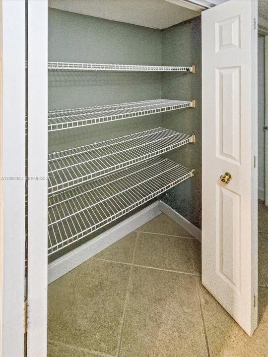 Storage closet featuring four tiers of white wire shelving and tile flooring