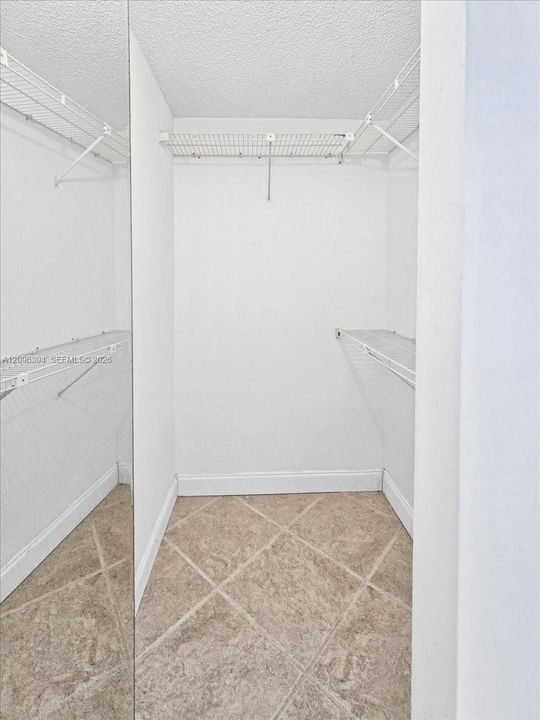 Walk-in storage space featuring full-length mirror paneling, white wire shelving, and neutral ceramic tile flooring