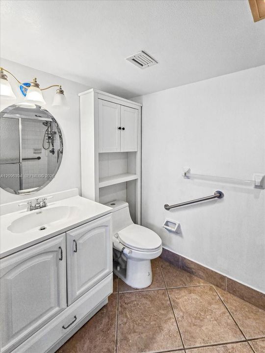 Bathroom featuring a white vanity with integrated sink, circular mirror, built-in floor-to-ceiling storage cabinetry, tile flooring, and metallic wall-mounted safety bars