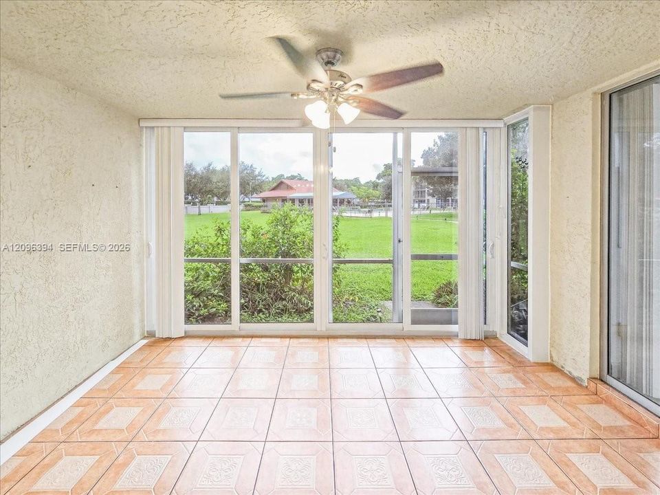Enclosed sunroom featuring ceramic tile flooring, textured ceilings, a multi-blade ceiling fan with integrated lighting, and expansive glass sliding door panels