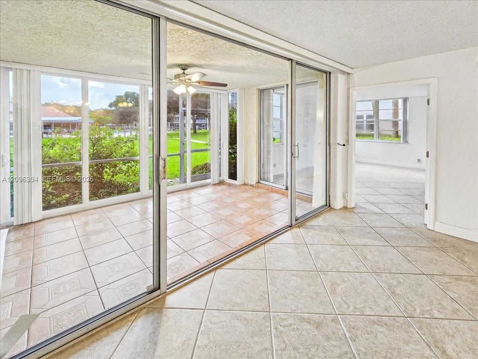 Enclosed sunroom featuring expansive glass sliding doors, neutral tile flooring, and a ceiling fan