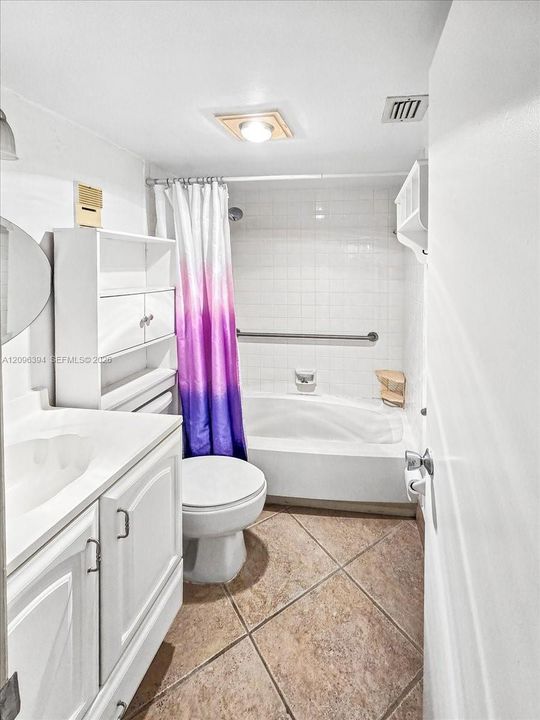 Bathroom featuring tile flooring laid on a diagonal, a white vanity with integrated basin, built-in cabinetry, and a tub with tile surround and wall-mounted grab bar