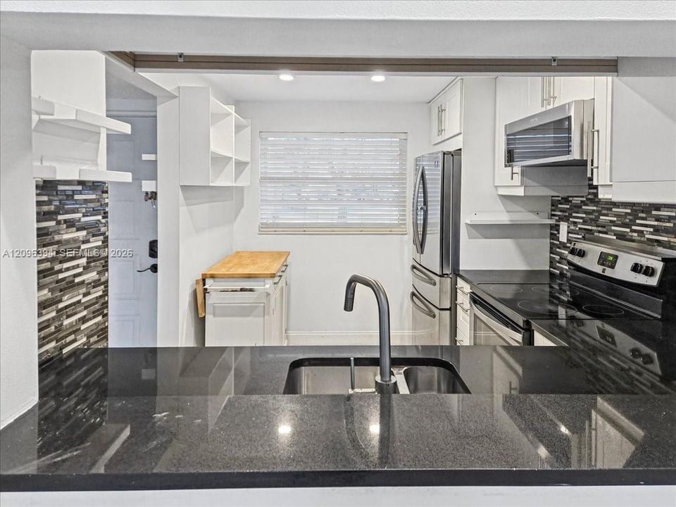 Kitchen featuring black stone countertops, a stainless steel dual-basin undermount sink with a high-arch faucet, white cabinetry, a multi-tone horizontal tile backsplash, and stainless steel appliances