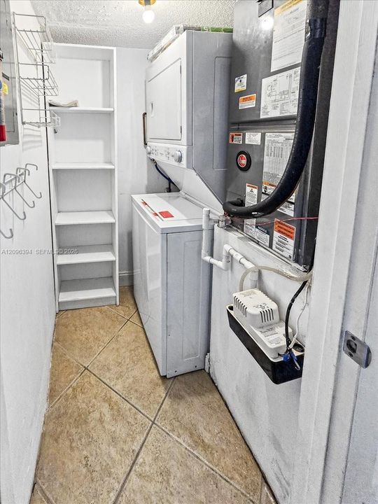 Utility space featuring ceramic tile flooring, built-in shelving, stackable laundry units, and mechanical climate control system