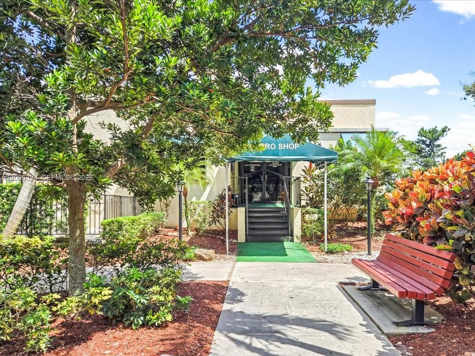 Building entrance featuring an awning-covered staircase, concrete walkway, and landscaped grounds with mature trees and shrubbery