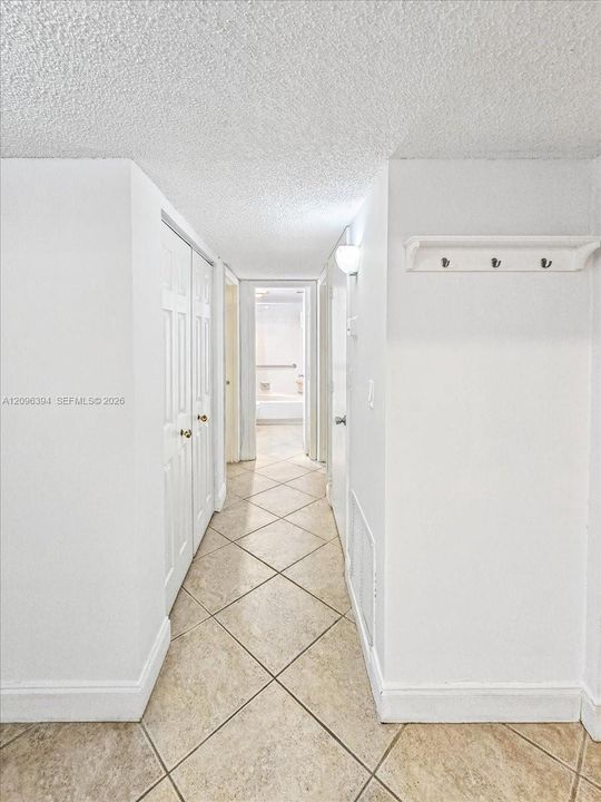 Hallway featuring neutral-toned tile flooring set on a diagonal, dual-panel closet doors, and a wall-mounted hook rack