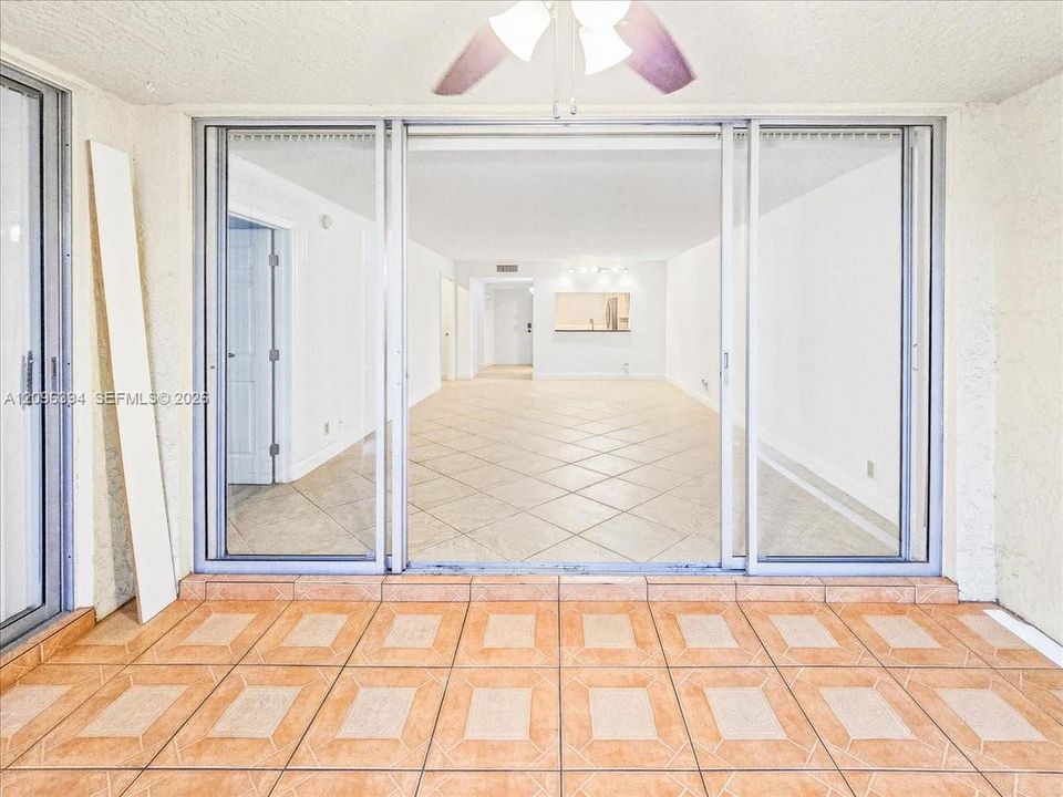 Triple-panel sliding glass doors with brushed metal frames, ceramic tile flooring, and ceiling fan with integrated lighting
