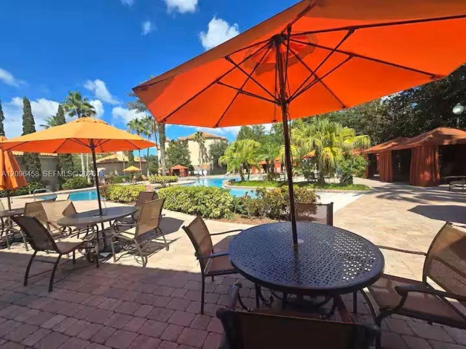 Outdoor terrace with interlocking paver hardscaping, swimming pool, mature palm trees, and permanent shaded cabana structures