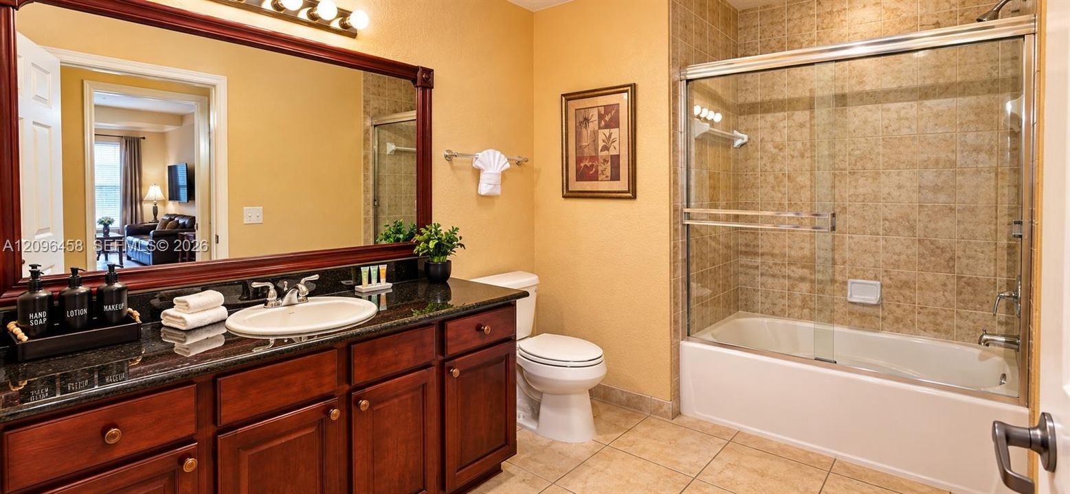 Bathroom featuring dark wood-finish cabinetry, a stone-surface countertop, an oval undermount sink, a framed vanity mirror, and a tiled tub-shower combination