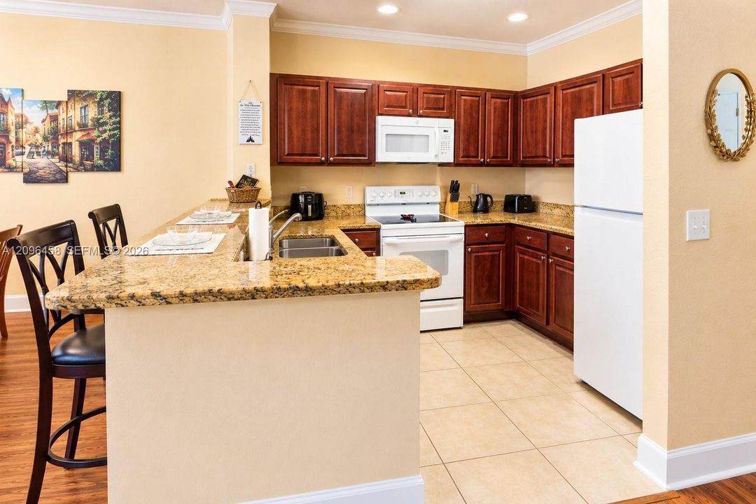 Kitchen featuring medium-toned wood cabinetry, stone-surface countertops, an integrated breakfast bar, white appliances, and tile flooring