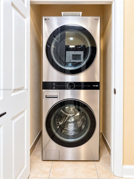 Stacked stainless steel laundry center featuring a front-load washer and dryer with integrated digital controls and tile flooring