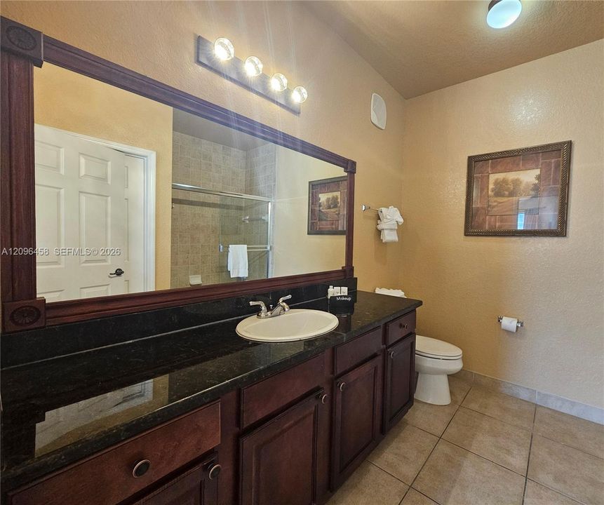 Vanity featuring dark-toned cabinetry, a dark stone countertop, an integrated oval sink, and a large wall-mounted mirror with a wood frame, complemented by tiled flooring