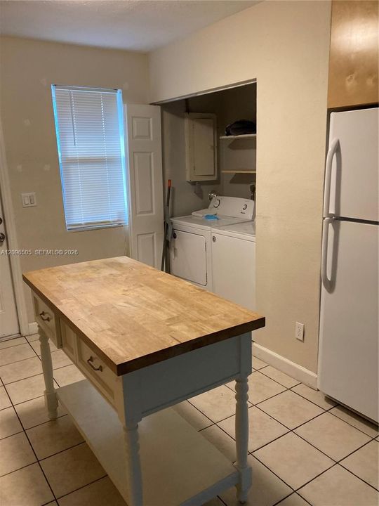 Built-in laundry area with shelving, tile flooring, and a kitchen island featuring a wood-finish countertop
