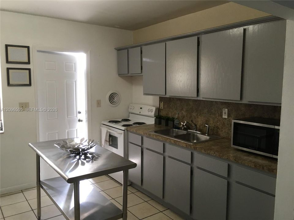 Kitchen featuring grey cabinetry, stone-finish countertops, dual-basin stainless steel sink, and ceramic tile flooring