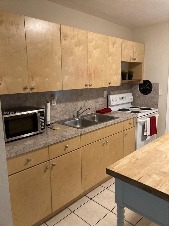 Light-toned wood cabinetry with round hardware, stone-finish laminate countertops, stainless steel dual-basin sink, and tile flooring
